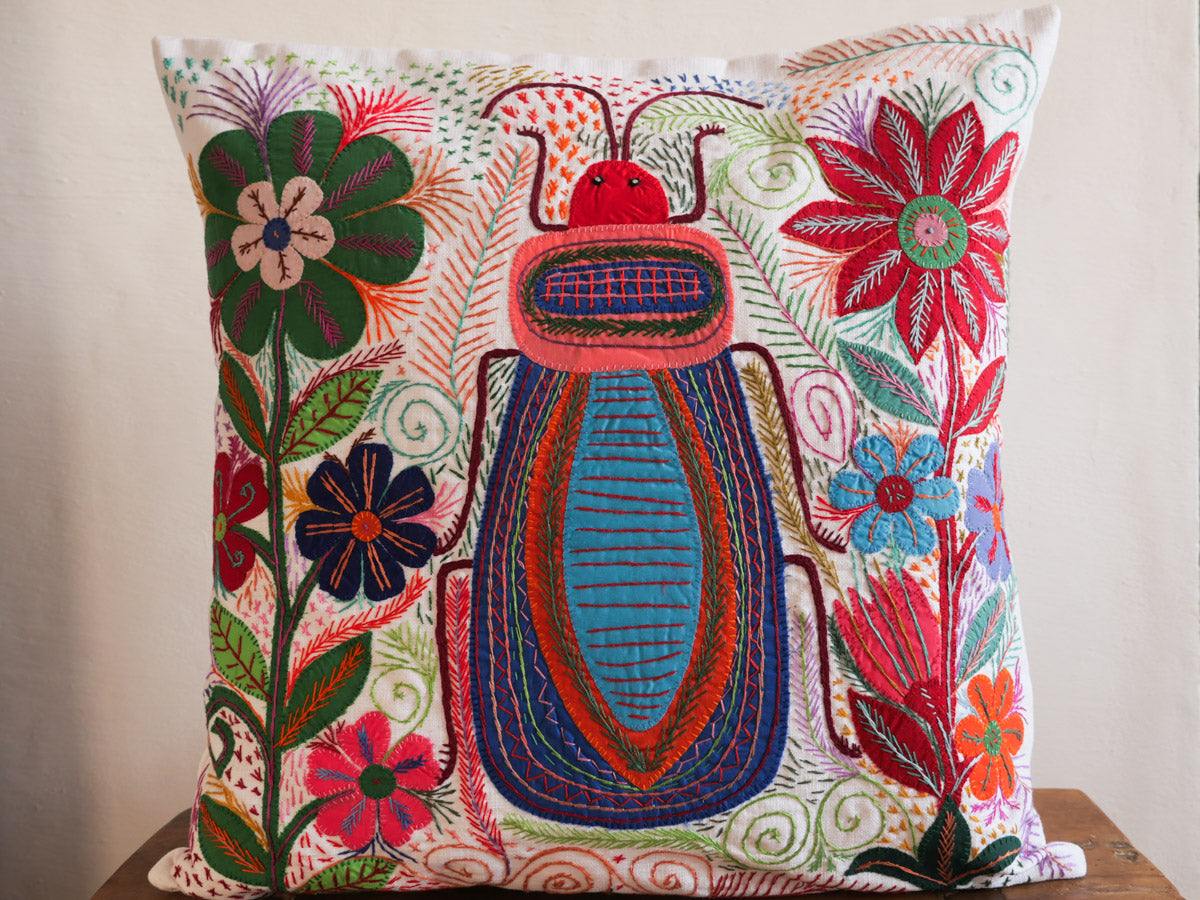Coussin brode main avec des motifs insectes et fleur, commerce equitable.