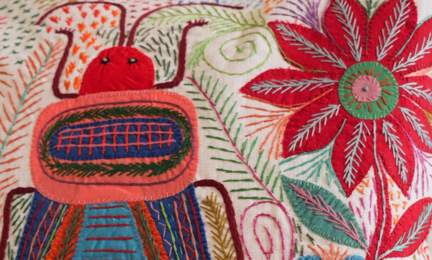 Coussin brode main avec des motifs insectes et fleur, commerce equitable.