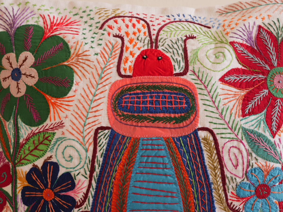 Coussin brode main avec des motifs insectes et fleur, commerce equitable.