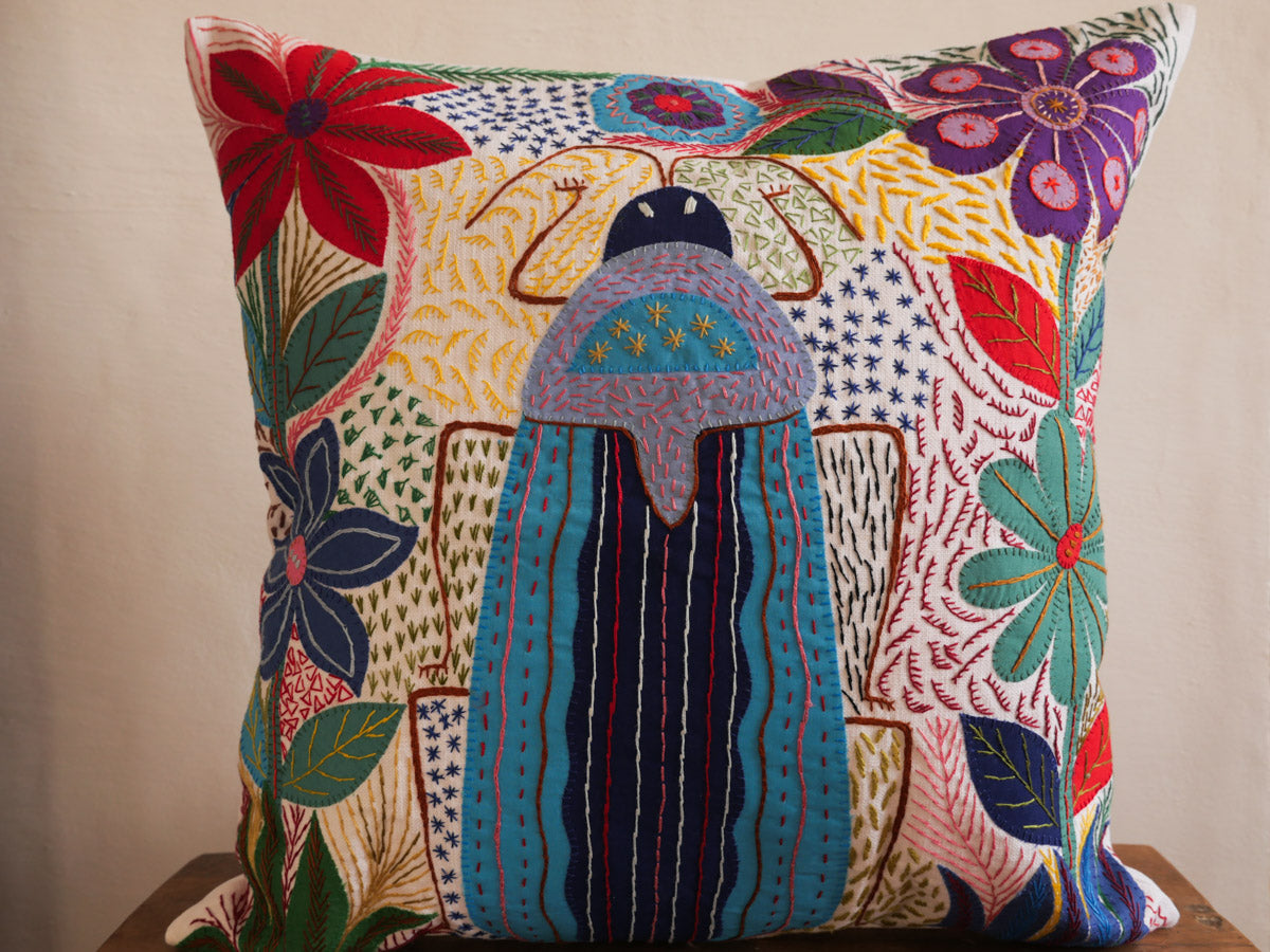 Coussin brode main avec des motifs insectes et fleur, commerce equitable.