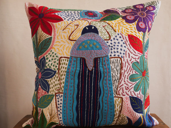 Coussin brode main avec des motifs insectes et fleur, commerce equitable.