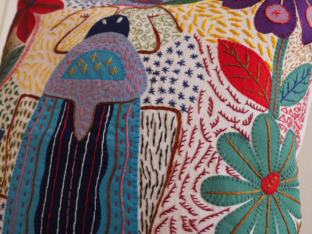 Coussin brode main avec des motifs insectes et fleur, commerce equitable.