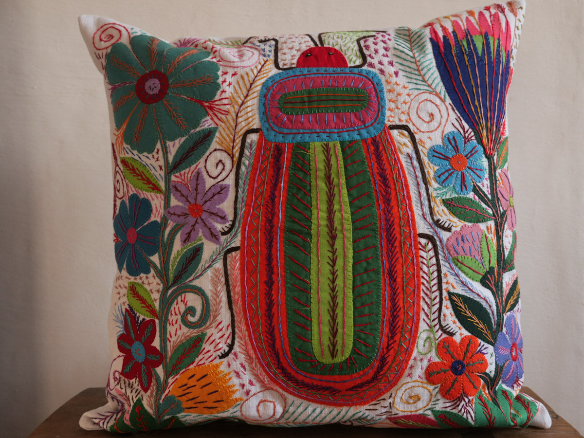 Coussin brode main avec des motifs insectes et fleur, commerce equitable.