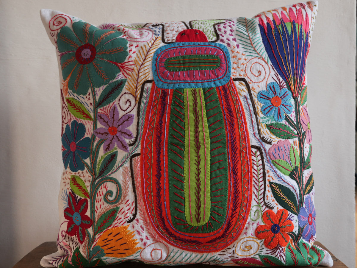 Coussin brode main avec des motifs insectes et fleur, commerce equitable.