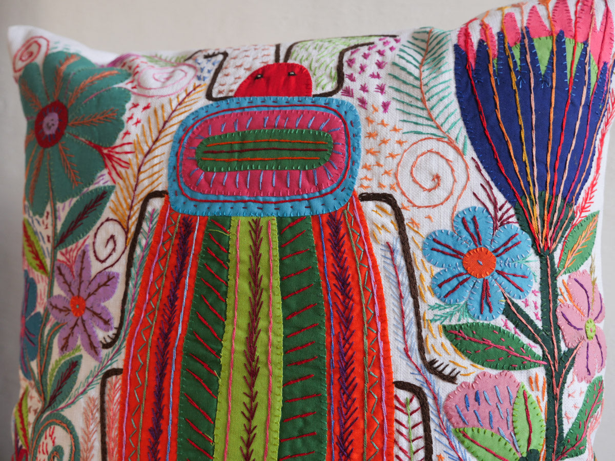 Coussin brode main avec des motifs insectes et fleur, commerce equitable.